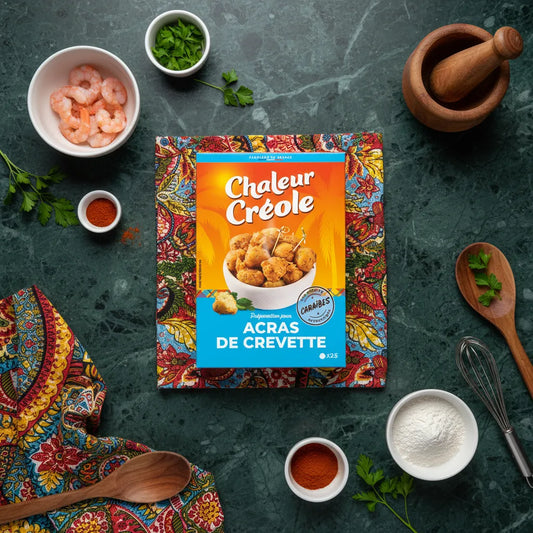 Boîte de préparation pour acras de crevette Chaleur Créole posée sur un tissu coloré, entourée d’ingrédients comme crevettes, farine et épices.