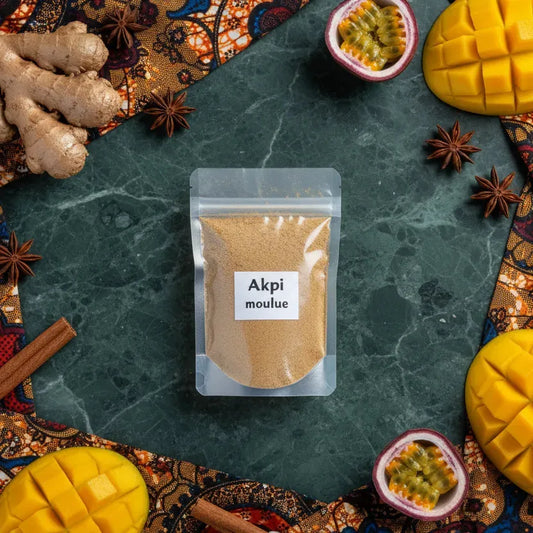 Sachet d’Akpi moulue Cameroun entouré d’ingrédients exotiques, épice ouest-africaine à texture fine pour cuisine savoureuse.
