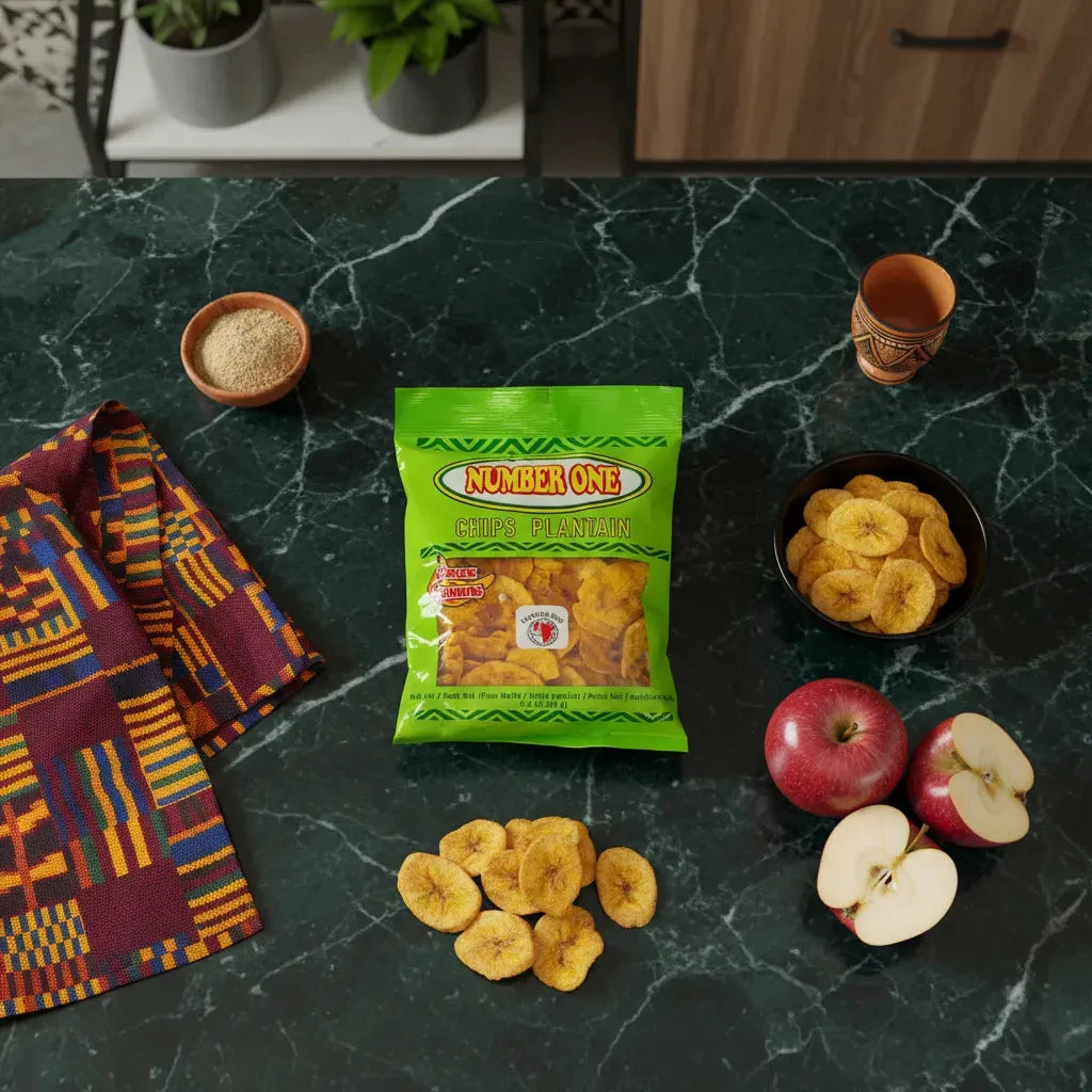 Chips de plantain pomme N°1 sur table en marbre avec pommes rouges, bol de chips et tissu coloré. Snack original et croustillant.