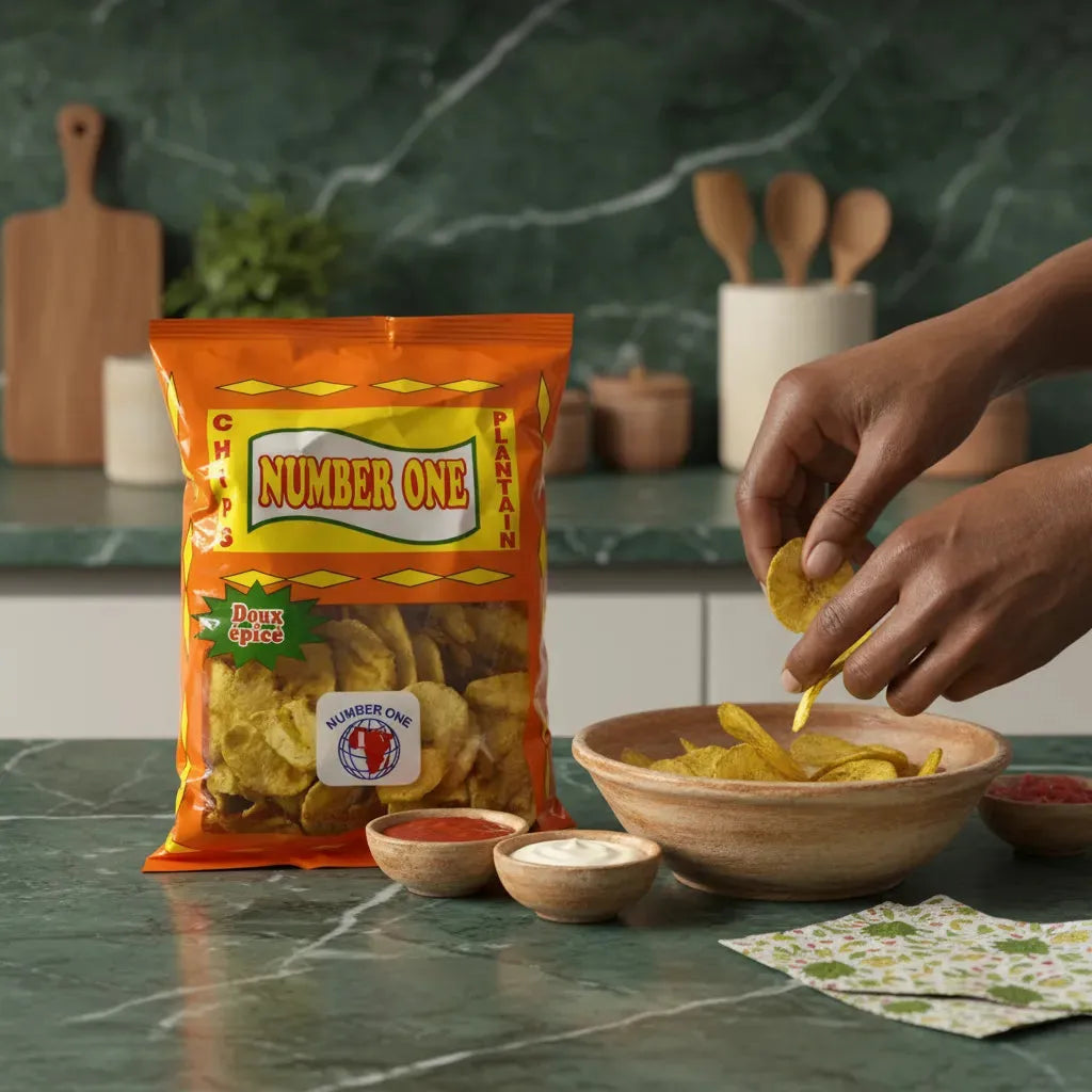 Main servant des Chips Plantain Épicées N°1 - Douces et Croustillantes dans un bol avec sauces, sur plan de travail vert. Produit phare en épicerie salée.