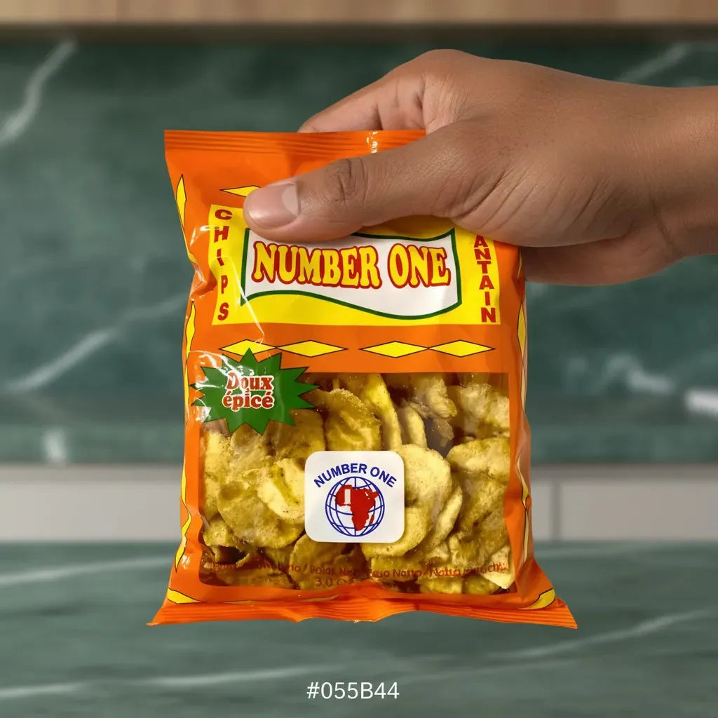 Main tenant un sachet de Chips Plantain Épicées N°1 - Douces et Croustillantes devant un fond de cuisine. Snack sucré-salé en épicerie salée.