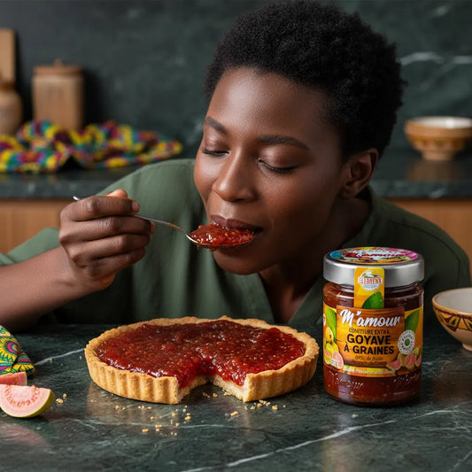 Femme dégustant une tarte garnie de confiture de goyave M'AMOUR, pot visible à côté, mettant en valeur la texture sucrée et fruitée du produit.