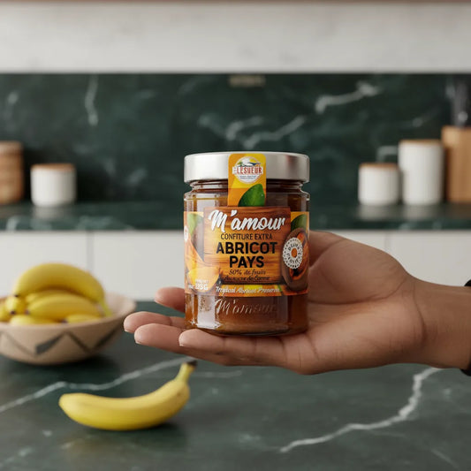 Main tenant un pot de confiture d'abricot pays M'AMOUR dans une cuisine moderne, produit d'épicerie sucrée aux fruits tropicaux visible en détail.