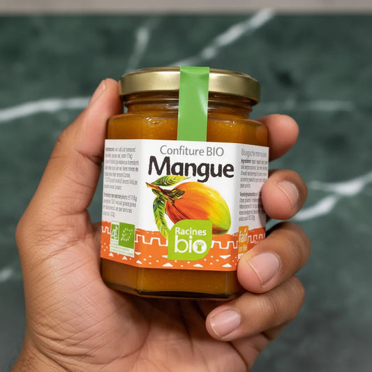 Main tenant un pot de confiture mangue RACINES BIO, étiquette verte et orange. Confiture bio à la mangue pour une touche exotique sucrée.