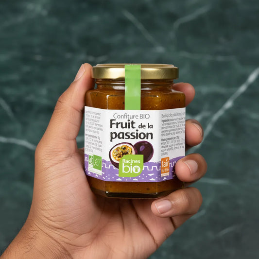 Main tenant un pot de confiture fruit de la passion bio Racines, produit issu de l'agriculture biologique, parfait pour tartines et desserts.