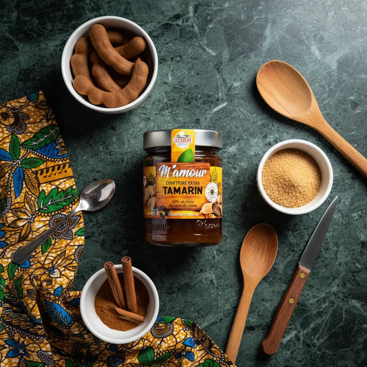 Confiture de tamarin M'AMOUR entourée d'ingrédients naturels comme tamarin, sucre de canne et cannelle, sur fond de marbre vert.