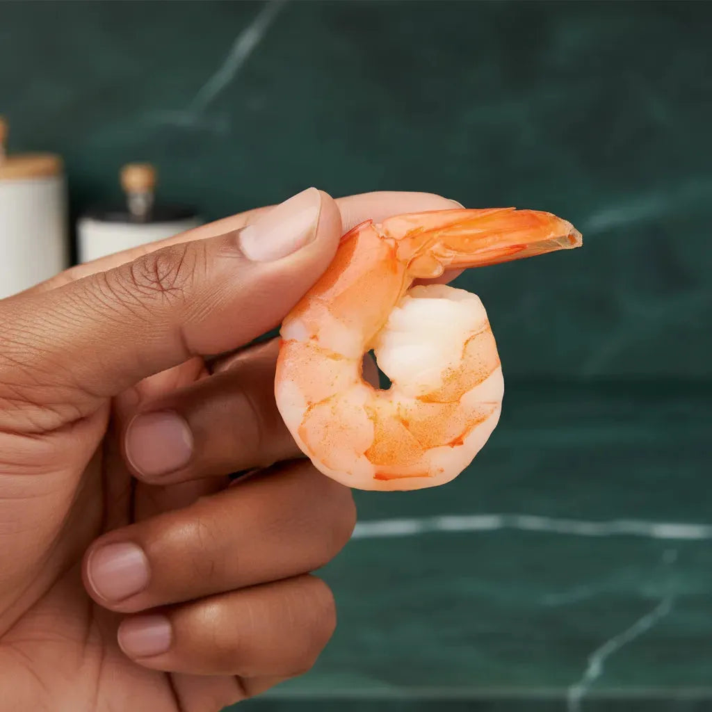 Crevette cuite décortiquée tenue à la main - Saveur et Praticité, prête à être dégustée, idéale pour apéritifs ou recettes rapides de fruits de mer.
