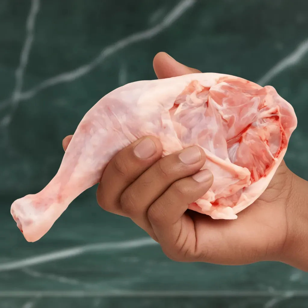 Main tenant une cuisse de poulet halal crue, viande fraîche et savoureuse. Produit surgelé de volaille conforme aux normes halal.