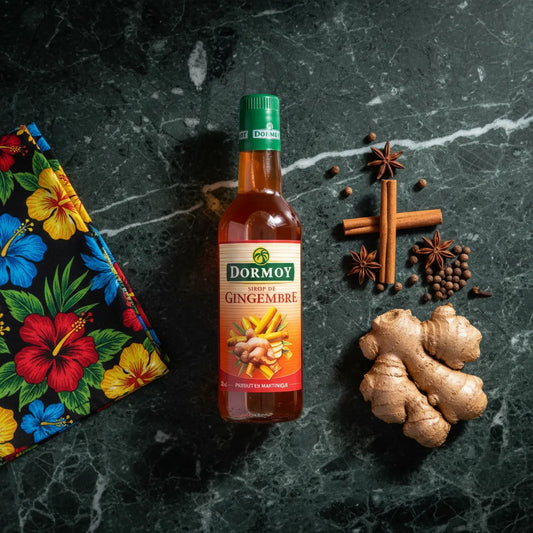 Sirop de gingembre Dormoy posé sur une table en marbre avec gingembre frais, cannelle et anis étoilé, parfait pour boissons et recettes exotiques.
