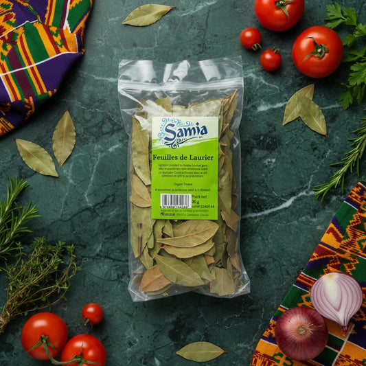 Sachet de feuilles de laurier SAMIA entouré d'ingrédients frais sur fond vert. Laurier séché pour rehausser les plats selon la tradition culinaire.