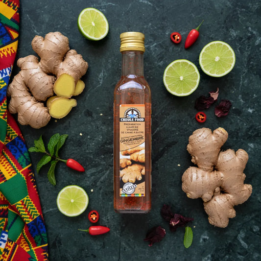 Bouteille de vinaigre de canne au gingembre CREOLE FOOD entourée de gingembre frais, citrons verts et piments sur fond tropical.