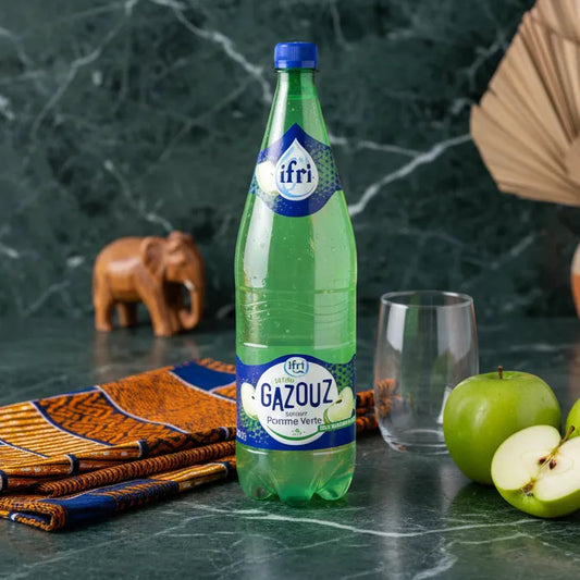 Soda Pomme Verte IFRI GAZOUZ posé sur une table avec pomme verte et verre vide, boisson pétillante parfaite pour accompagner un repas.