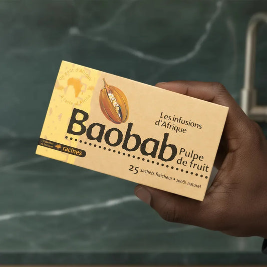 Main tenant une boîte d'infusion Baobab Racines, soulignant son format pratique et ses ingrédients 100% naturels aux vertus nutritionnelles.