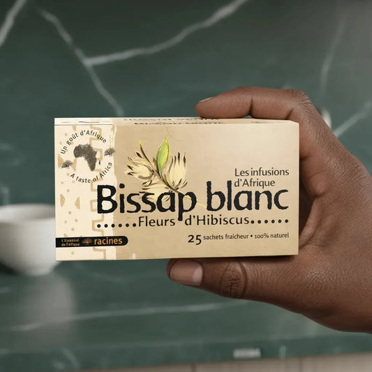 Main tenant une boîte d'infusion bissap blanc RACINES, 25 sachets aux fleurs d'hibiscus, boisson naturelle et rafraîchissante d'Afrique.