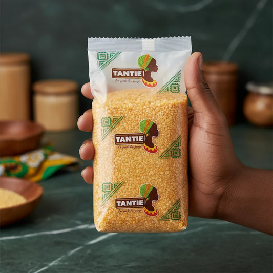 Main tenant un sachet de maïs Haïti broyé TANTIE, produit d’épicerie salée à texture granuleuse pour cuisine créole ou fusion.