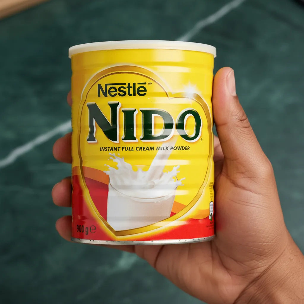 Main tenant une boîte de lait en poudre NIDO 900g, produit laitier essentiel pour la cuisine et les boissons familiales.