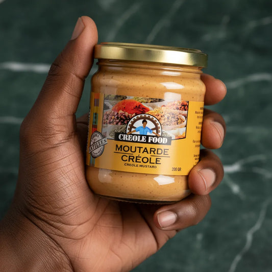 Main tenant un pot de moutarde créole CREOLE FOOD 200g, condiment épicé aux saveurs créoles pour accompagner plats de viande ou poisson.