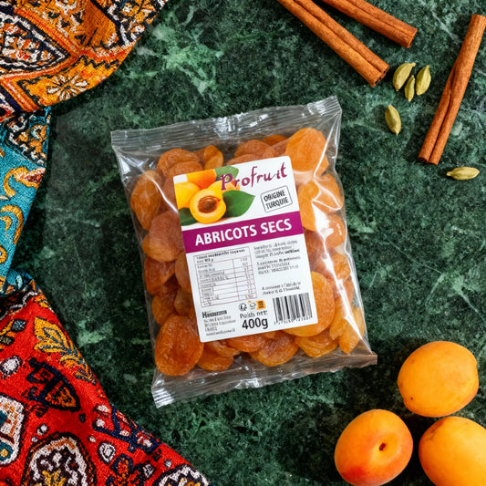 Sachet d'abricots secs PROFRUIT 400g posé sur table verte avec épices et fruits frais, idéal pour recettes sucrées orientales.