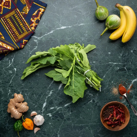 Feuilles d'aubergine africaines posées sur une table avec épices, gingembre, ail et légumes, idéales pour cuisine africaine.