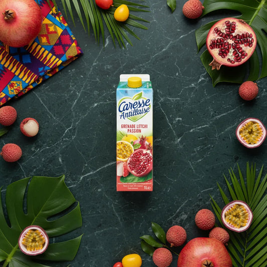 Brique de nectar Grenade Letchi Passion Caresse Antillaise entourée de fruits frais tropicaux, mise en scène colorée pour boisson exotique.