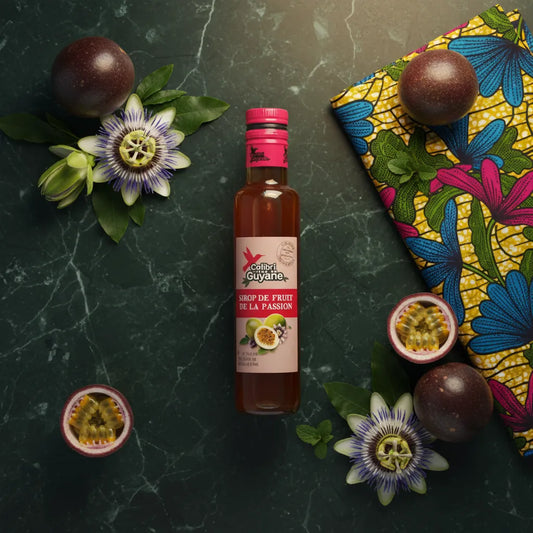 Bouteille de sirop passion DELICES DE GUYANE entourée de fruits de la passion et fleurs exotiques, évoquant les saveurs de la Guyane.