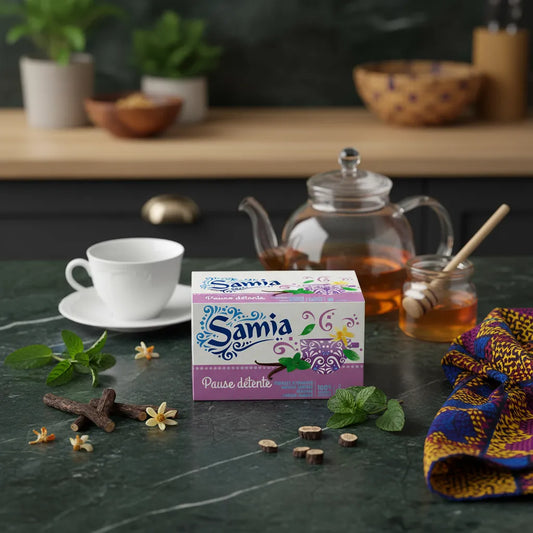 Boîte d'infusion détente SAMIA posée sur une table avec théière, tasse, miel, menthe, réglisse et fleurs, illustrant les ingrédients naturels.