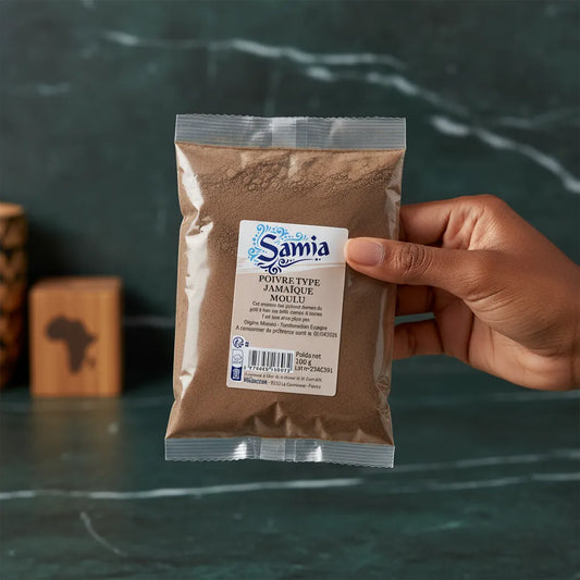 Main tenant un sachet de poivre moulu type Jamaïque SAMIA, épice fine et parfumée pour assaisonnement raffiné en cuisine.