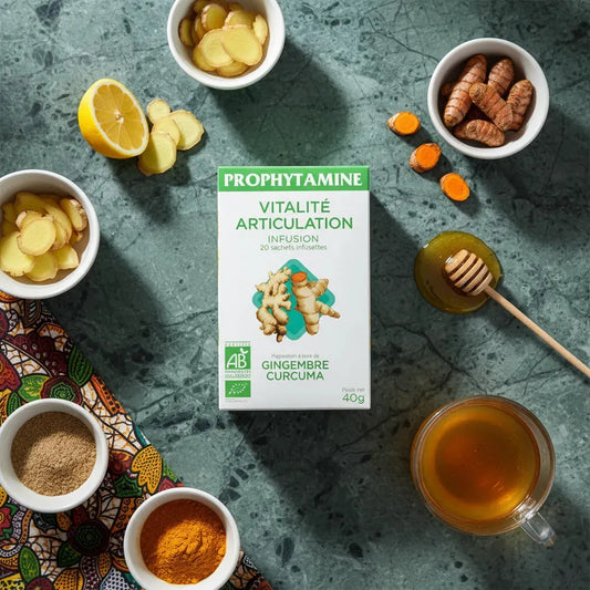 Infusion articulation bio PROPHYTAMINE entourée d'ingrédients naturels comme gingembre, curcuma, citron et miel sur table en marbre.