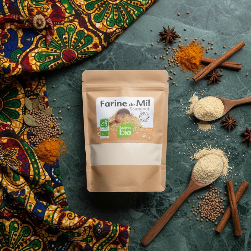 Farine de Mil RACINES BIO posée sur une table avec épices et tissu africain, ingrédient naturel pour cuisine traditionnelle et bio.