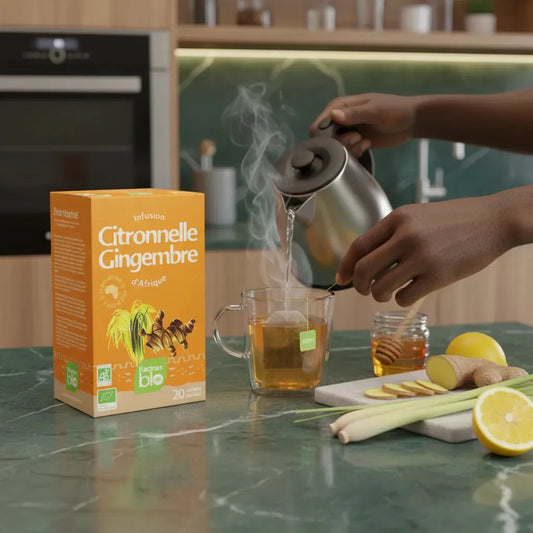 Préparation d'une tasse d'infusion citronnelle gingembre bio RACINES avec eau chaude, citron, miel et citronnelle sur plan de travail.