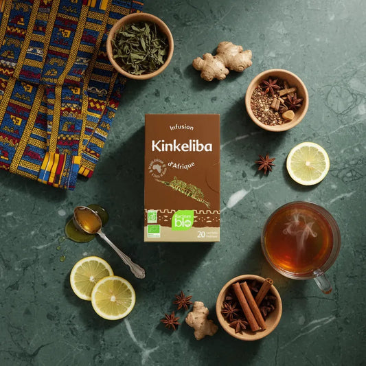 Infusion kinkeliba BIO Afrique Racines entourée d'ingrédients naturels comme citron, gingembre et cannelle, sur fond vert marbré.