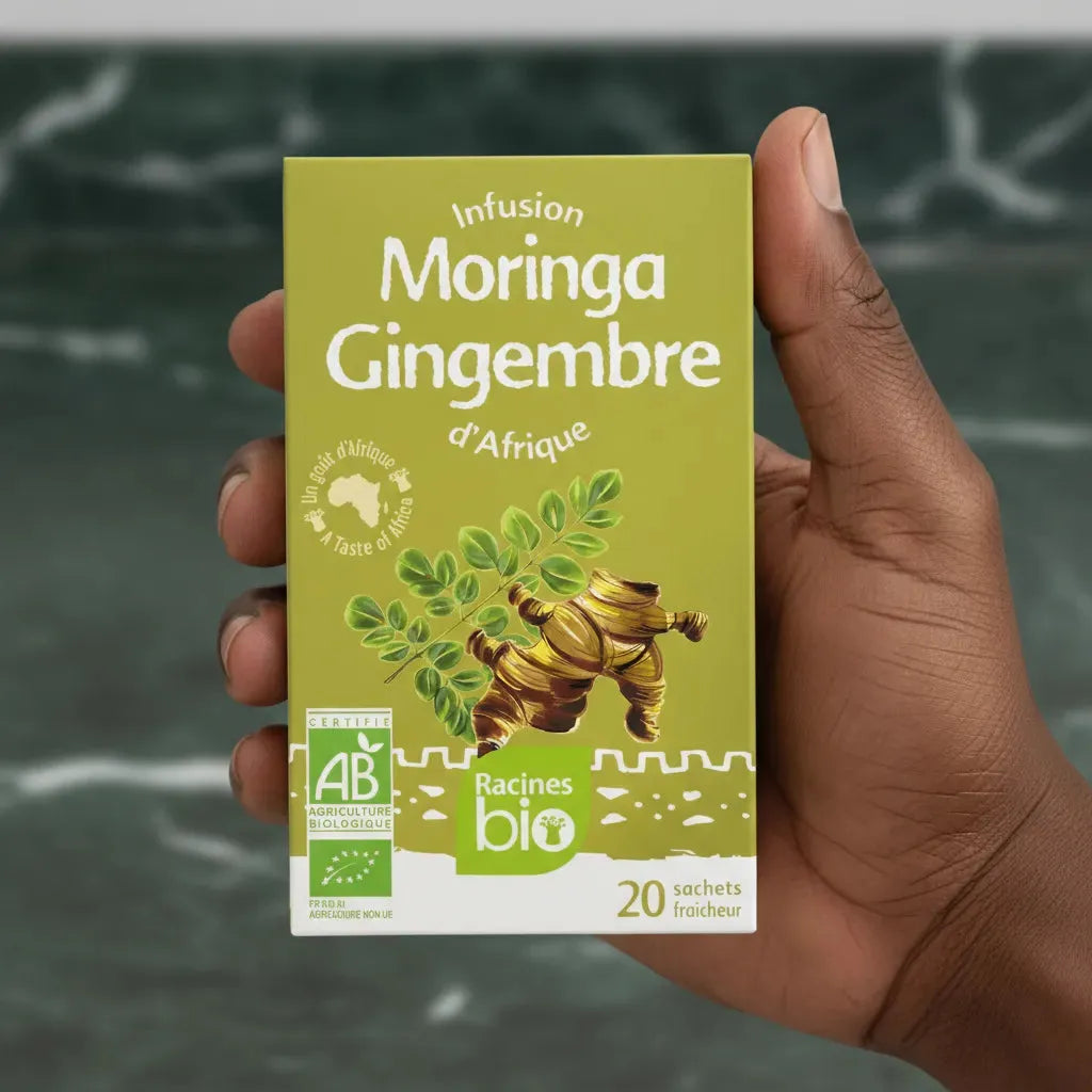 Main tenant une boîte d'infusion gingembre moringa BIO Racines, produit bio bien-être à base de plantes africaines, 20 sachets fraîcheur.