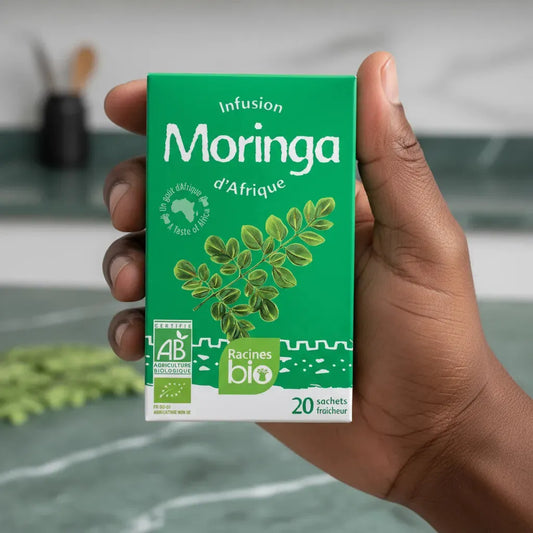 Main tenant une boîte d'infusion Moringa Bio RACINES, 20 sachets fraîcheur, produit bio aux vertus nutritionnelles africaines.