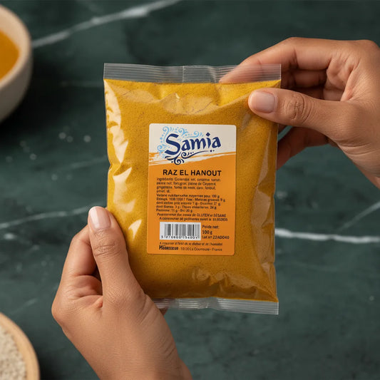 Main tenant un sachet de Raz el Hanout SAMIA, mélange d'épices pour plats traditionnels, étiquette visible en gros plan.