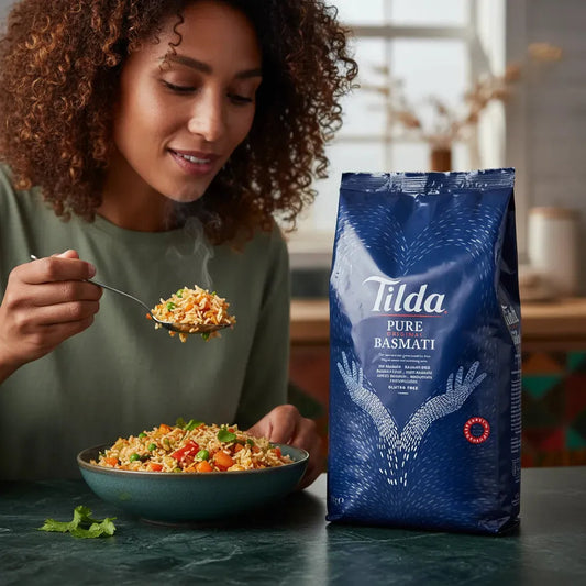 Femme dégustant un plat de riz cuisiné avec le Riz Basmati TILDA, sac de riz visible sur la table, parfait pour plats savoureux maison.