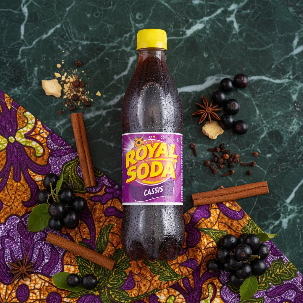 Bouteille de ROYAL SODA Cassis posée sur tissu coloré avec épices et fruits noirs, boisson gazeuse au goût riche et authentique de cassis.