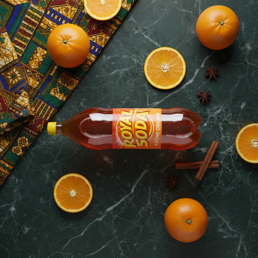 ROYAL SODA goût orange posé sur une table en marbre entouré d’oranges fraîches et d’épices, illustrant sa saveur naturelle et authentique.