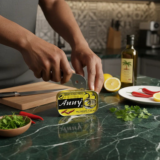 Main ouvrant une boîte de sardines épicées ANNY sur un plan de travail avec citron, piments rouges et herbes fraîches, ambiance culinaire épicée.