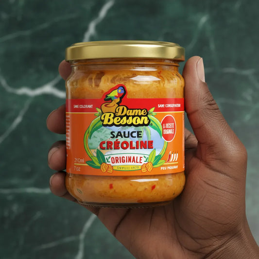 Main tenant un pot de sauce créoline DAME BESSON - Épicée, texture onctueuse, idéale pour relever les plats créoles et exotiques.