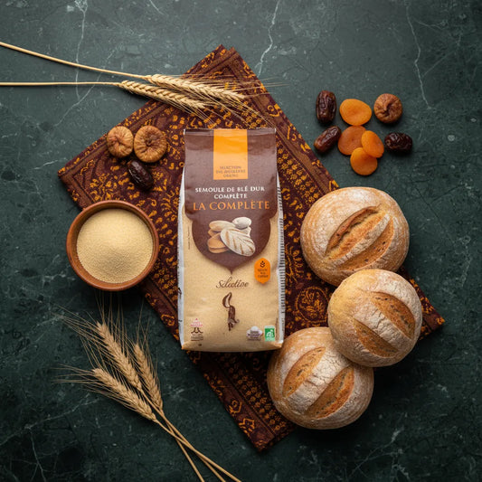 Semoule de blé complet RENARD posée sur table avec pains ronds, fruits secs et épis de blé. Produit naturel pour recettes riches en nutriments.