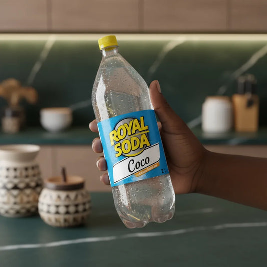 Main tenant une bouteille de soda coco ROYAL SODA 2L, boisson gazeuse exotique à la noix de coco dans une cuisine contemporaine.