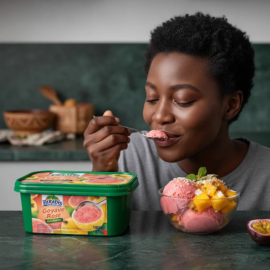 Femme dégustant une glace goût goyave PARADIS GLACE avec un bol de sorbet rose garni de mangue, dans une cuisine moderne.