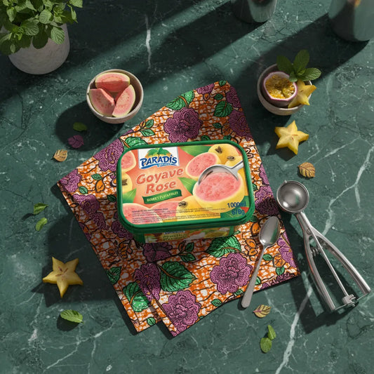 Bac de glace goût goyave PARADIS GLACE posé sur un tissu coloré avec fruits tropicaux et cuillères, ambiance exotique et gourmande.