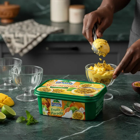 Main servant une boule de glace Paradis Maracudja dans une coupe, pot de sorbet passion visible, ambiance fraîche et fruitée en cuisine.