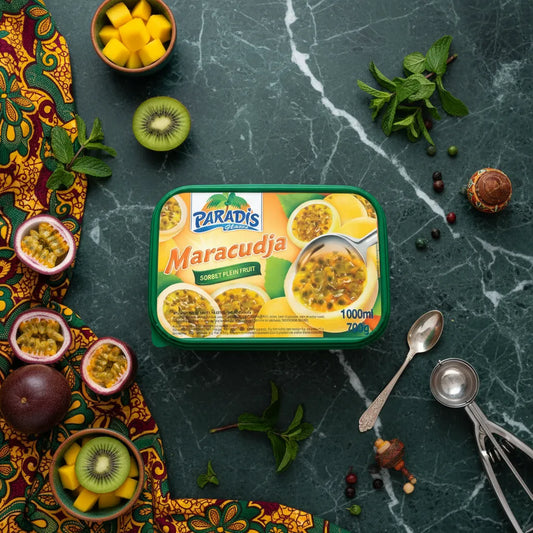 Pot de glace Paradis Maracudja sur table en marbre vert, entouré de fruits frais comme kiwi, mangue et fruit de la passion, ambiance tropicale.