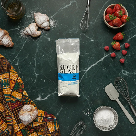 Sucre glace GIRAUDON 1 kg sur table de cuisine avec ustensiles et viennoiseries, parfait pour recettes de pâtisserie maison.