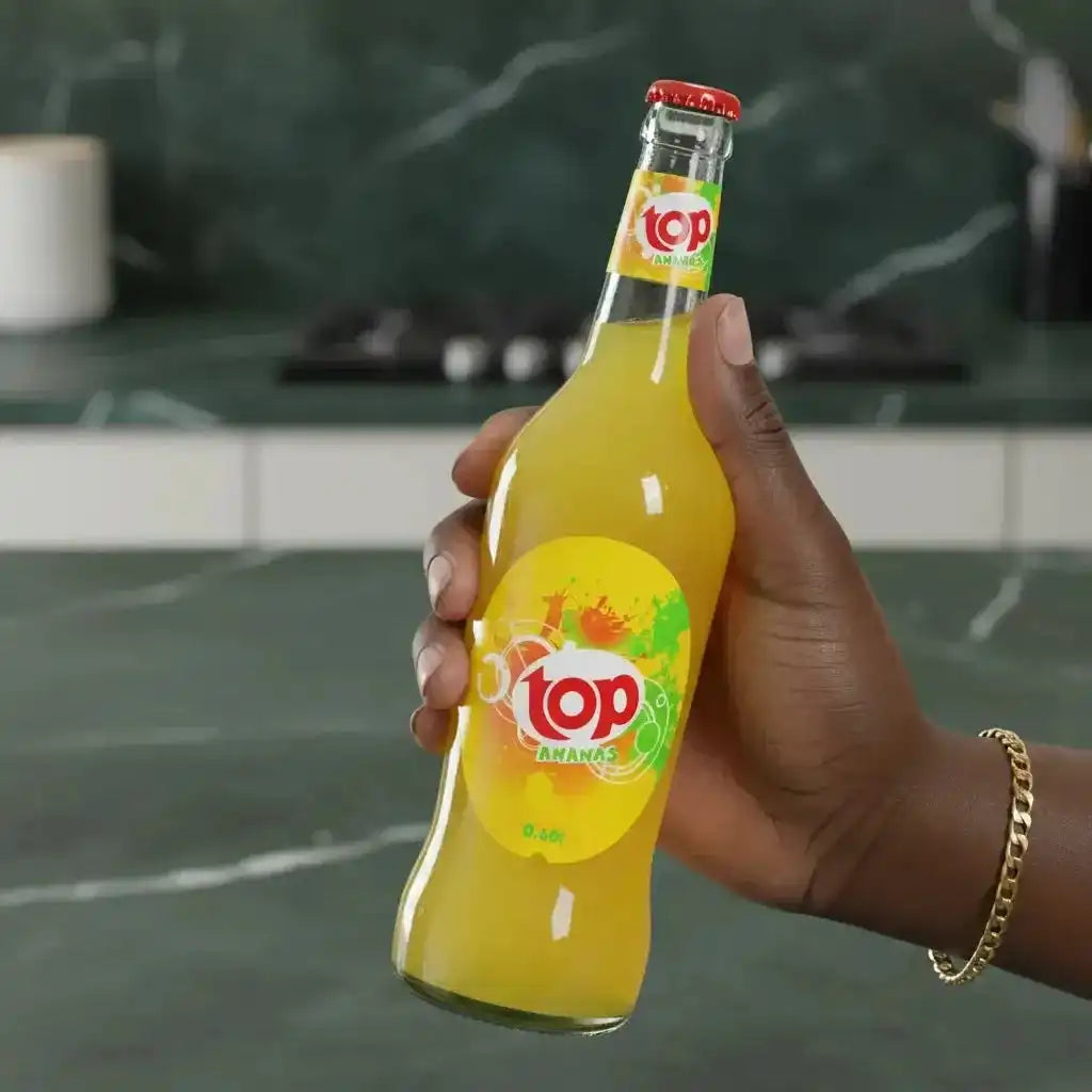 Main tenant une bouteille de Soda ananas TOP 0,6L, boisson gazeuse tropicale au goût d’ananas, parfaite pour une pause fruitée et pétillante.