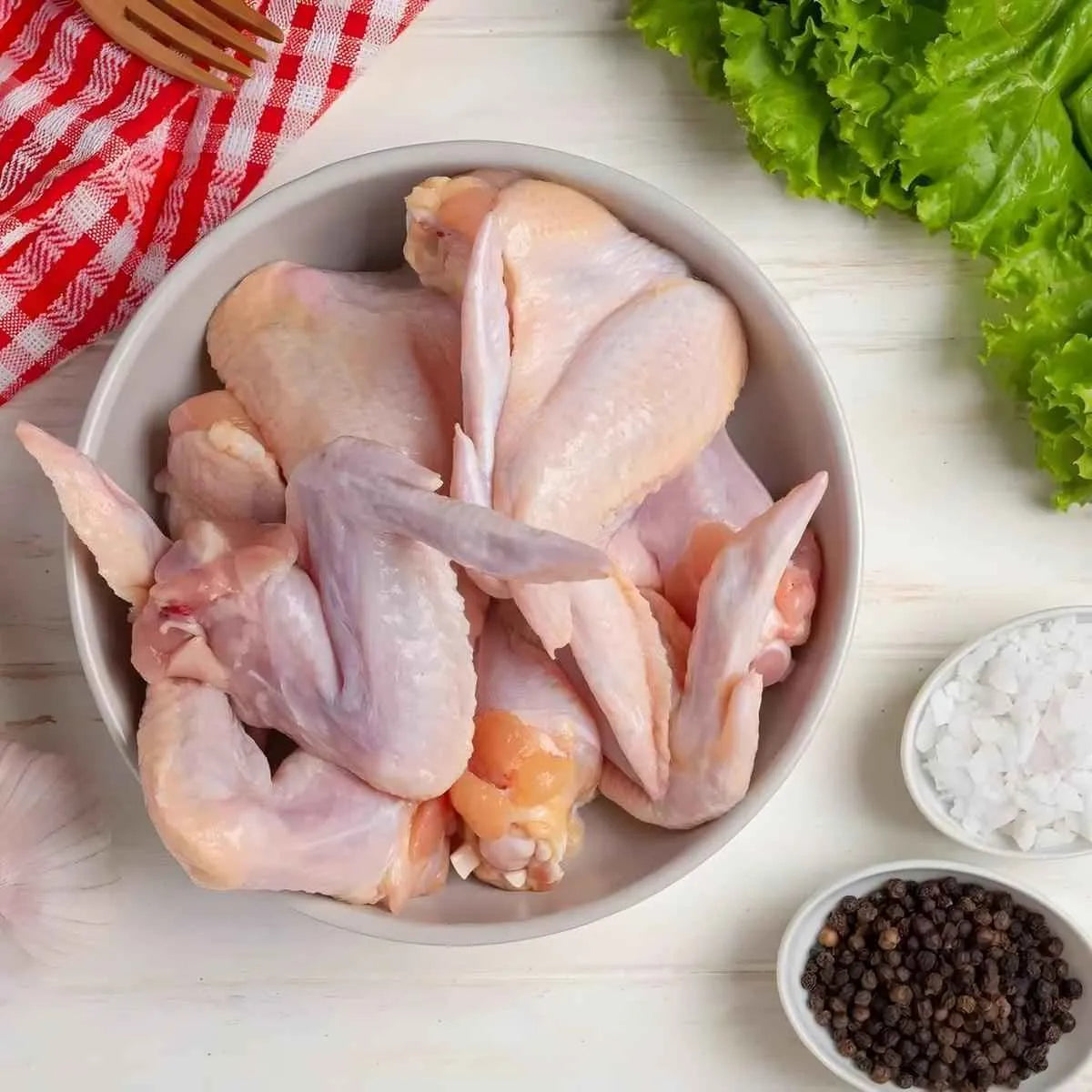 Ailerons de dinde nature surgelés dans un bol, entourés d’ingrédients frais. Convient pour recettes savoureuses de volaille.