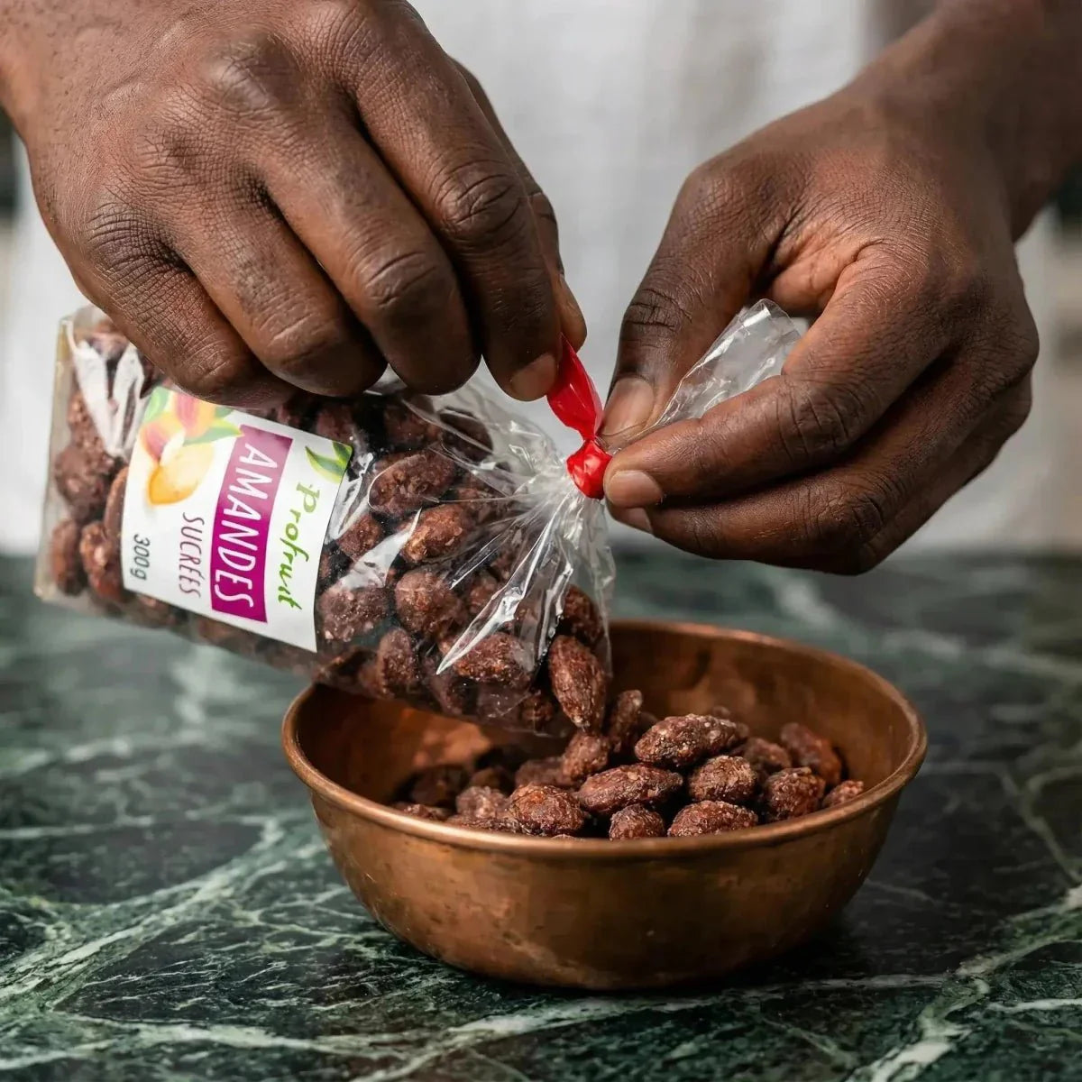 Mandorle zuccherate ProFruit 300g versate in una ciotola di rame su sfondo di marmo verde.