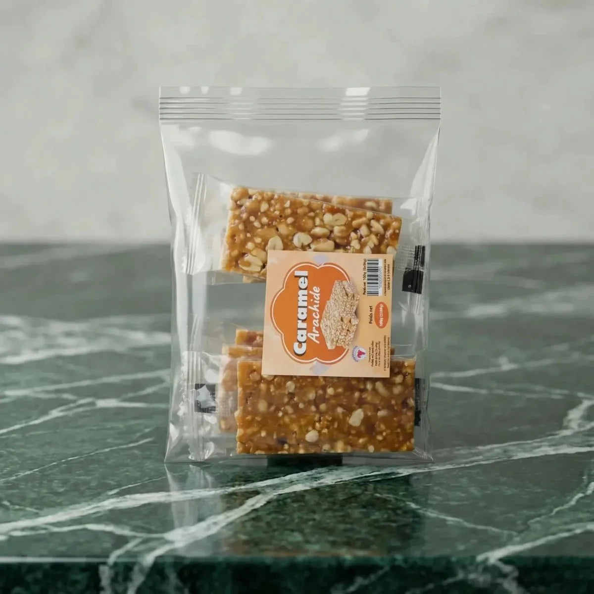 Barras de cacahuete caramelizado "Caramelo de Cacahuete" en bolsa transparente sobre fondo marmoleado verde.